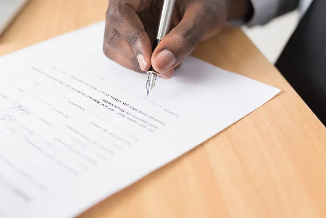 Persona firma un documento sobre una mesa de madera
