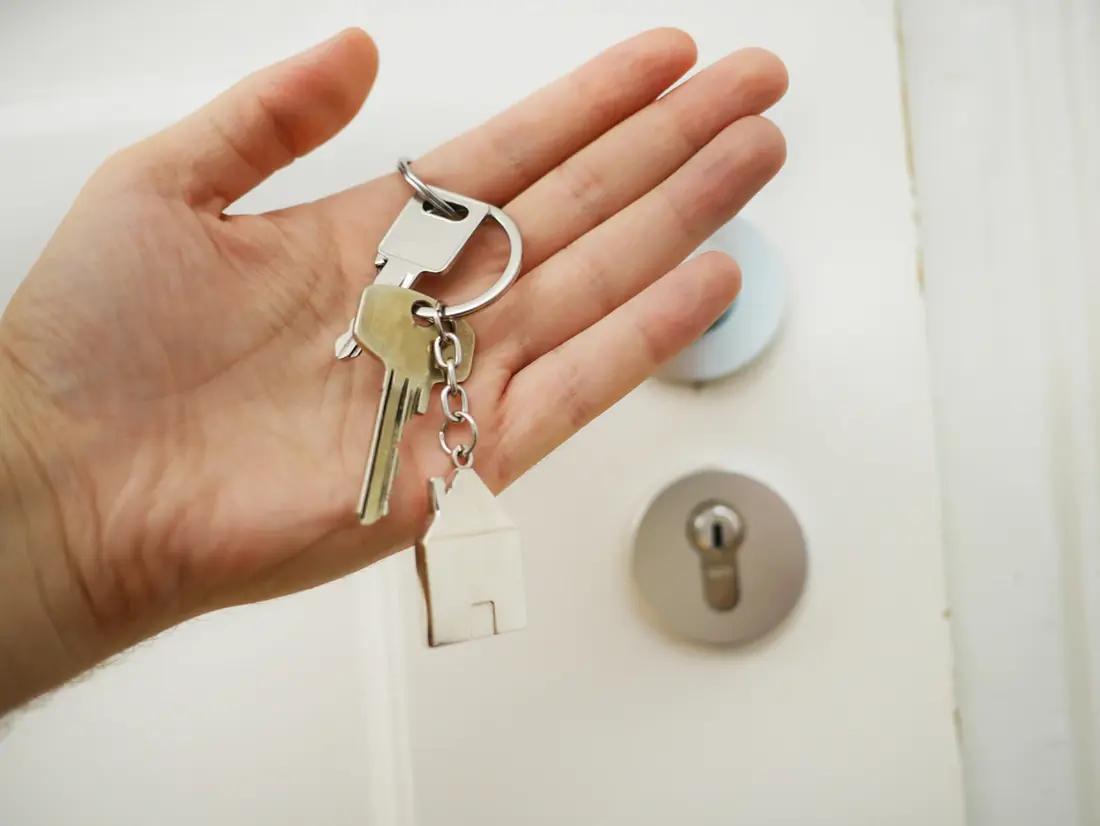 Mano que entrega las llaves de una vivienda junto a la cerradura de la puerta
